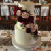 Hochzeitstorte - Rote Dahlien zieren neben den rosa Rosen und Olivenblättern die dreistöckige weiß eingestrichene Torte.