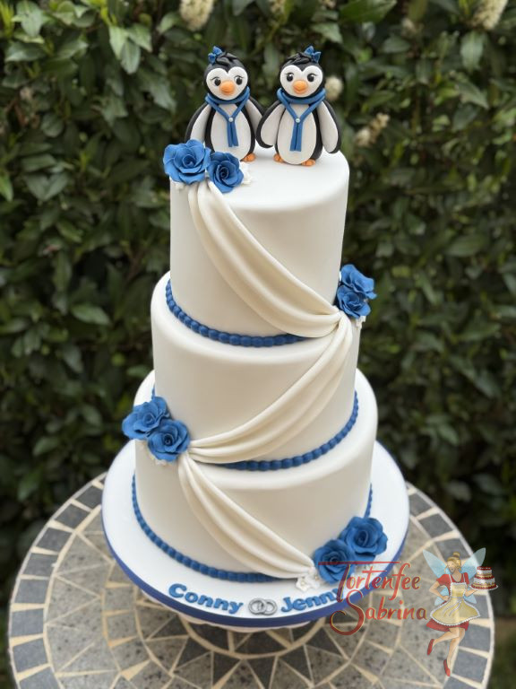 Hochzeitstorte - Verliebte Pinguine zieren ganz oben die dreistöckige Torte, mit auf der Torte sind zarte blaue Rosen.