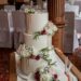 Hochzeitstorte - Weiss mit goldenem Drip auf der dreistöckigen Torte welche im Bereich des Drips mit Blumen verziert wurde.