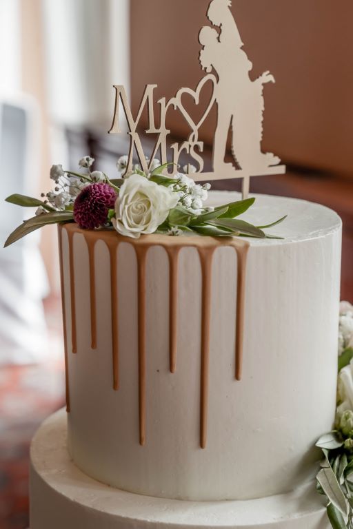 Hochzeitstorte - Weiss mit goldenem Drip auf der dreistöckigen Torte welche im Bereich des Drips mit Blumen verziert wurde.