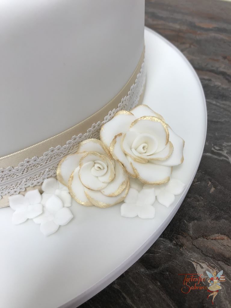 Hochzeitstorte - Weiß und Gold mit weißen Rosen welche goldene Blattspitzen haben, Abschluss der Torte mit gold/weißem Spitzenband