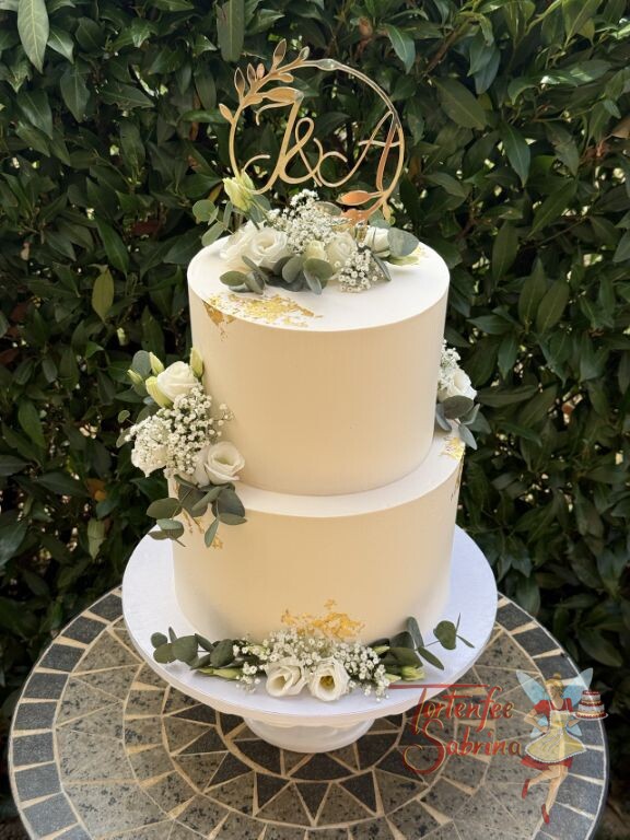 Hochzeitstorte - Weiße Blüten mit Blattgold verzieren neben dem goldenen Caketopper mit den Anfangsbuchstaben die Torte.
