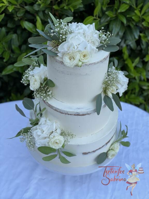 Hochzeitstorte - Weiße Blumen und grüne Blätter wurden auf der 3-stöckigen an verschiedenen Stellen drapiert.