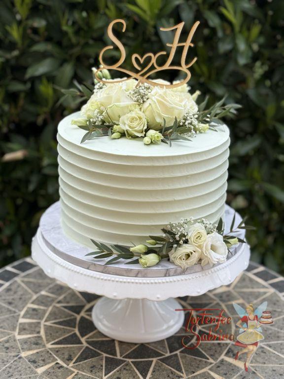 Hochzeitstorte - Weiße Rillen verzieren seitlich die Torte, oben bilden Rosen, Blattgrün sowie der Caketopper aus Holz den Abschluß.