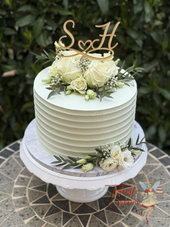 Hochzeitstorte - Weiße Rillen verzieren seitlich die Torte, oben bilden Rosen, Blattgrün sowie der Caketopper aus Holz den Abschluß.