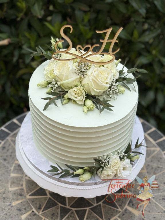 Hochzeitstorte - Weiße Rillen verzieren seitlich die Torte, oben bilden Rosen, Blattgrün sowie der Caketopper aus Holz den Abschluß.
