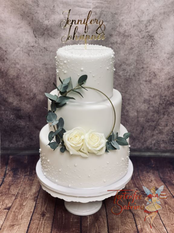 Hochzeitstorte - Weiße Zuckerperlen verschönern den obersten und untersten Stock der Torte, dazwischen ein goldener Ring mit Blumen.