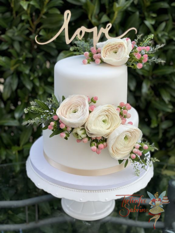 Hochzeitstorte - Zart rosa Ranunkeln in verschiedenen Größen, ganz oben ziert die Torte ein Cake Topper mit der Aufschrift Love.