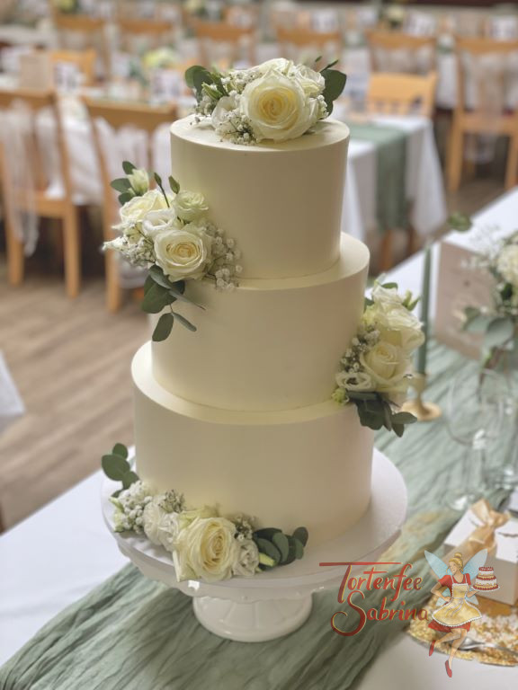 Hochzeitstorte - Zarte grüne Blätter des Eykalyptus zieren neben weissen Rosen die dreistöckige in weiß eingestrichene Torte.