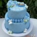 Tauftorte - Baby auf blauer Decke mit weißer Haube und Windel, die Torte wurde mit seitlich mit einem Rautenmuster und Perlen verziert.