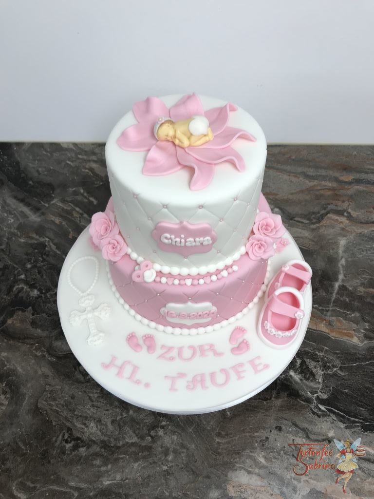 Tauftorte - Baby in rosa Blüte. Die Torte ist 2-stöckig mit Rautenmuster und Perlen verziert. Dekoriert mit Schuhen, Blumen und Kreuz.