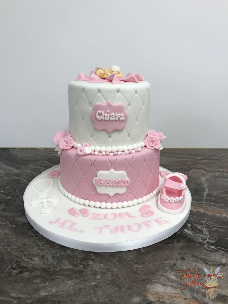 Tauftorte - Baby in rosa Blüte. Die Torte ist 2-stöckig mit Rautenmuster und Perlen verziert. Dekoriert mit Schuhen, Blumen und Kreuz.