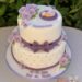 Tauftorte - Baby mit lila Marienkäferflügel, liegt auf der Torte auf einem Deckchen. Ebenfalls auf der Torte Rosen.