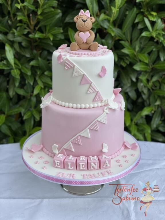 Tauftorte - Bärchen mit Herz und Schleife ganz oben auf der Torte, geschmückt mit einer rose und weißen Wimpelkette.