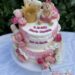 Tauftorte - Goldene Korne und Bärchen mit rosa Schleife sitzen oben auf der Torte umgeben von vielen Süßigkeiten.