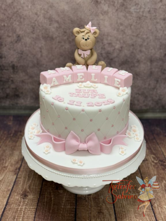 Tauftorte - Teddybär mit rosa Schleife sitzt ganz oben auf der Torte vor den kleinen Würfeln mit den Namen des Täuflings.